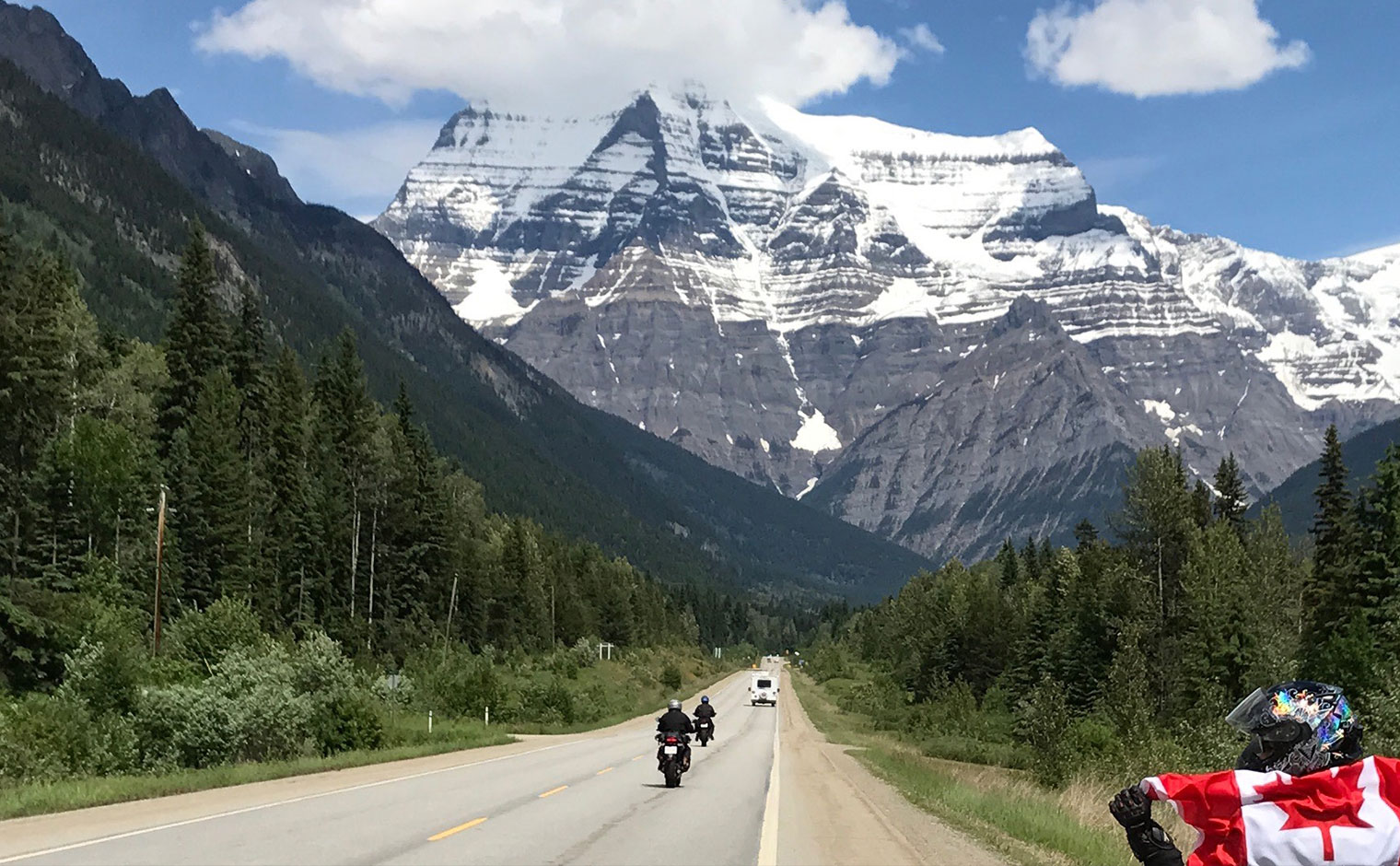 Mount Robson, the highest point in the Canadian Rockies, looming over motorcyclists riding down Route 16
