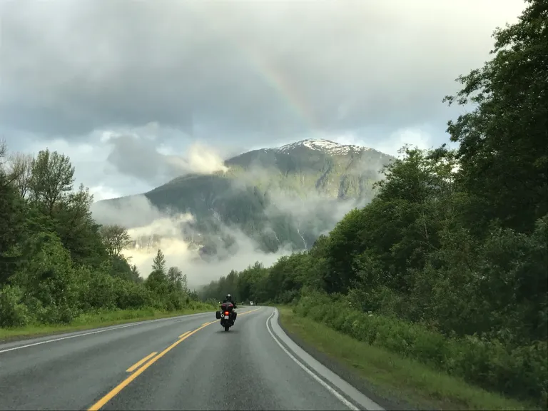 Motorcyclist riding Route 16 with cloud covered mountains and a rainbow over Highway 16